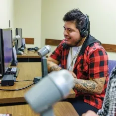 Two students wearing headphones observing a social work exercise with microphones and computers.